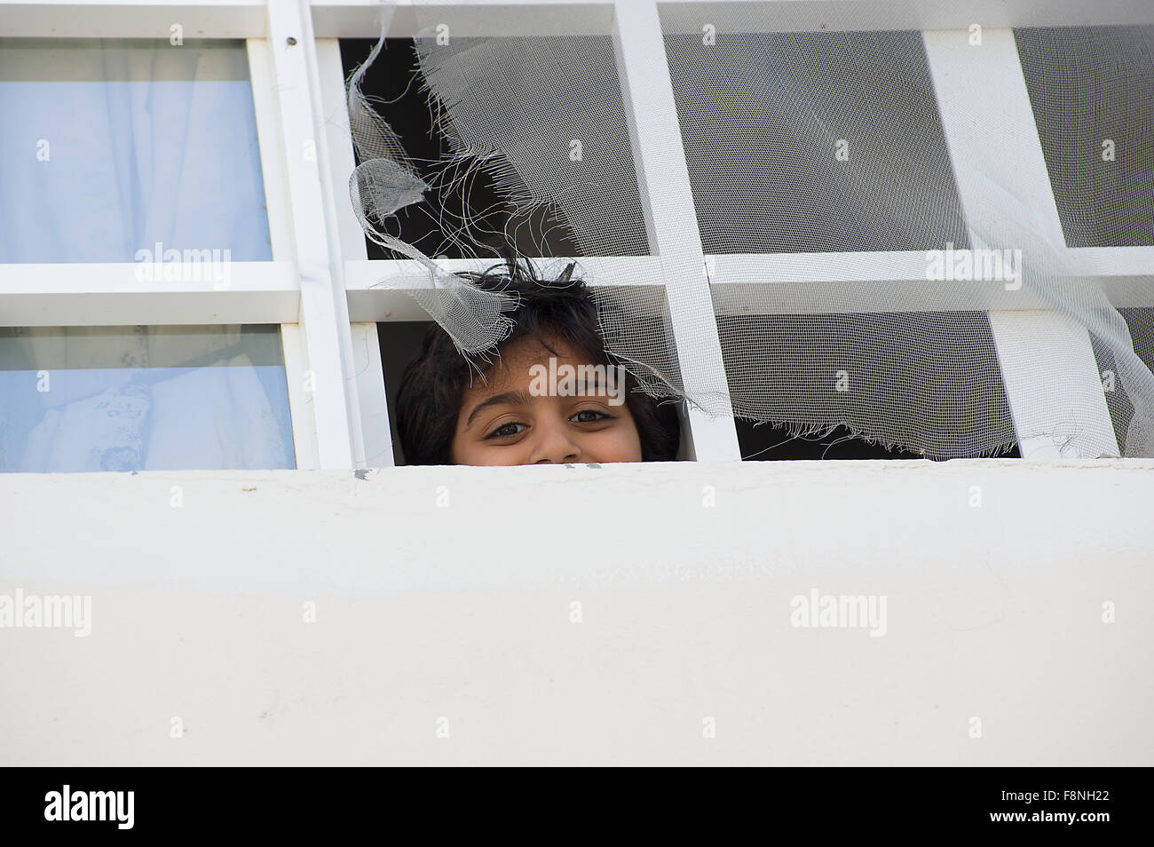 Boy in Oman hand peers with a smile out of a window with torn screens Stock Photo