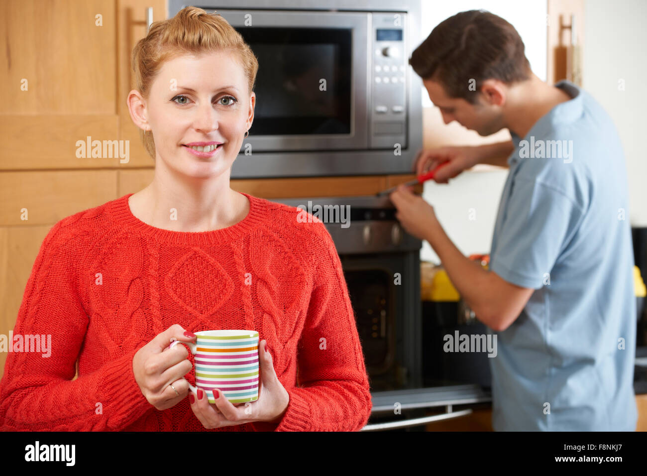 Woman Smiling As Cooker Is Repaired Stock Photo