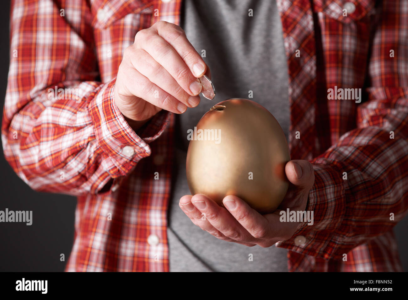 Man Putting Money Into Golden Egg Shaped Money Box Stock Photo
