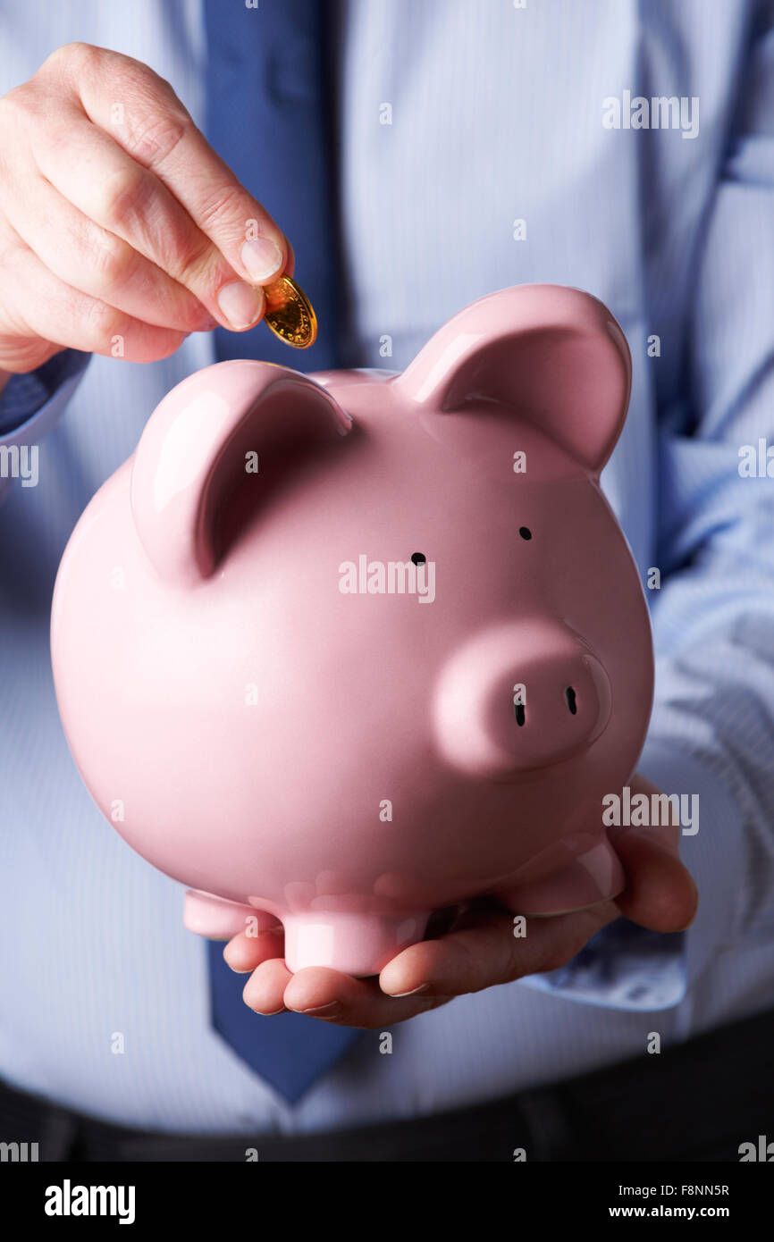 Businessman Putting Coin Into Large Piggy Bank Stock Photo - Alamy