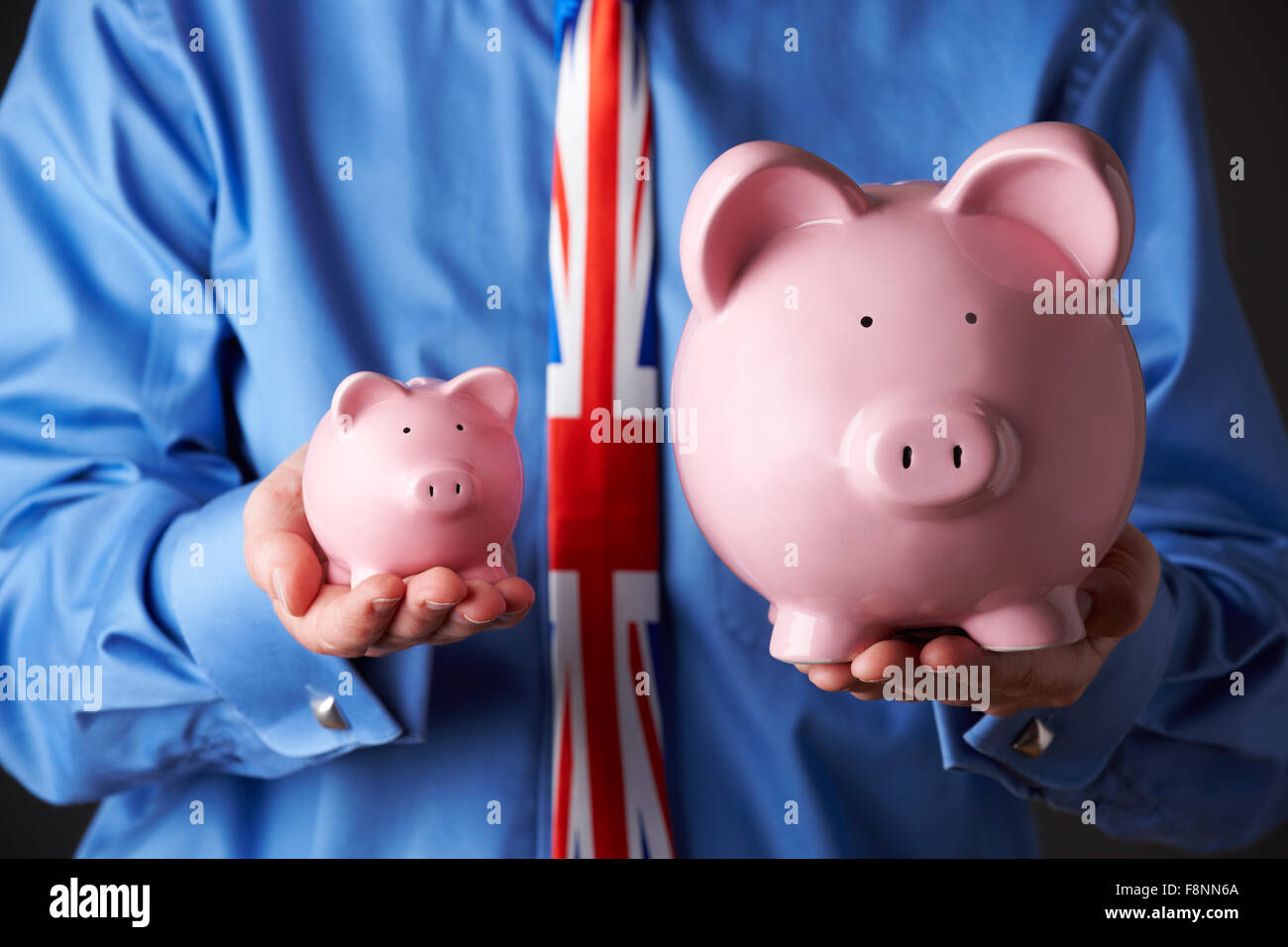 British Businessman Holding Large And Small Piggy Bank Stock Photo