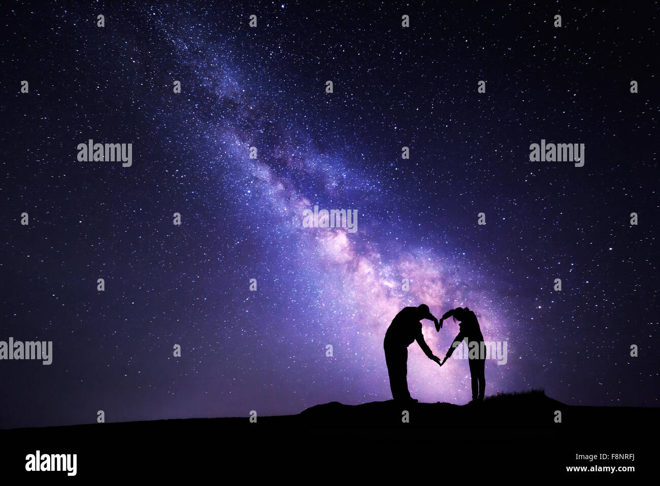 Man and woman holding hands in heart shape on the background of the Milky Way Stock Photo