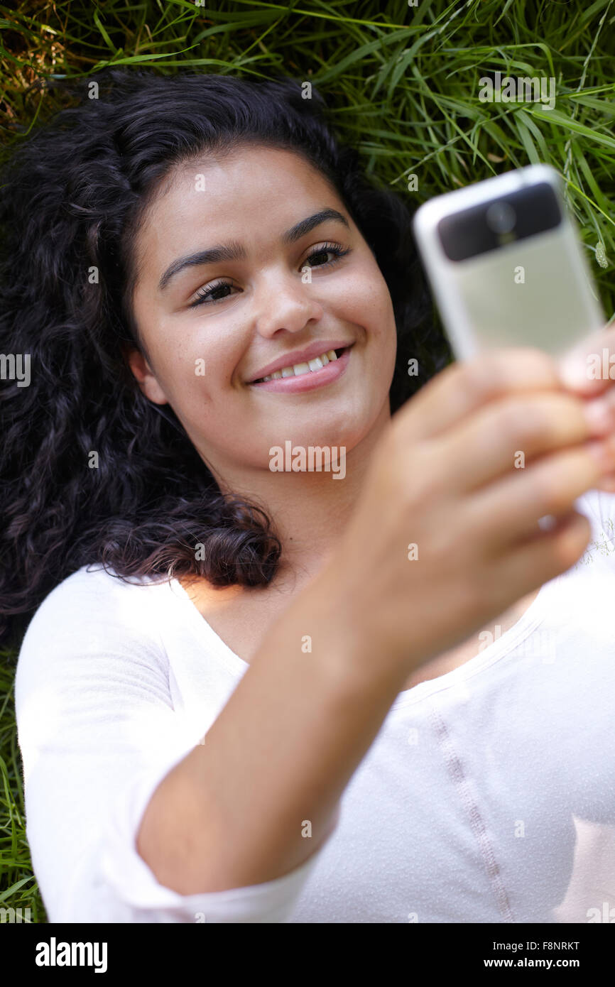 Young Woman Lying On Grass Sending Text Message Stock Photo