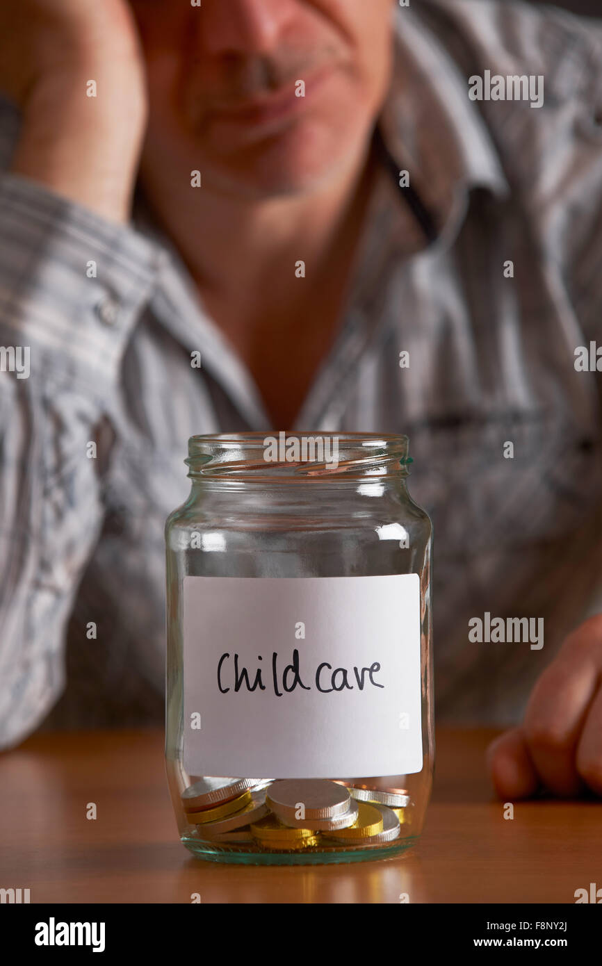 Depressed Man Looking At Empty Jar Labelled Childcare Stock Photo