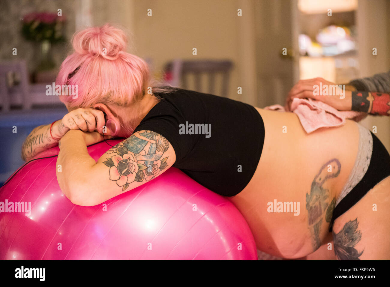 Woman in labour leaning on a yoga ball and having an ice pack held to her back by her partner at an unassisted home birth Stock Photo