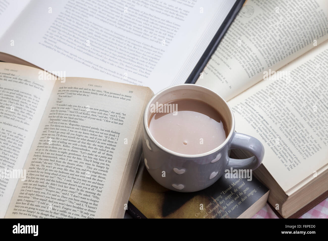 Mug of tea on tabletop covered with books Stock Photo