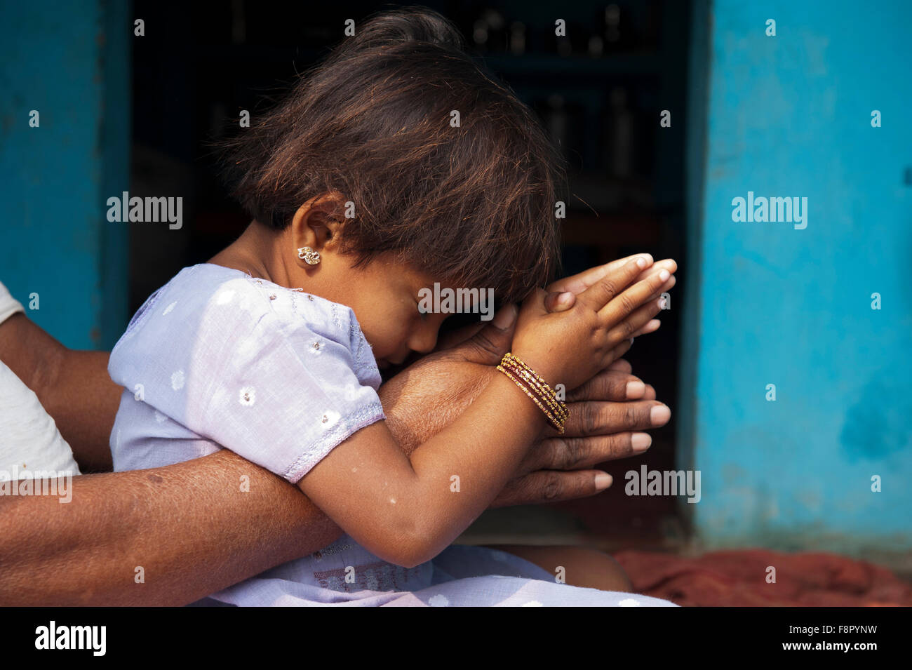 Indian girl sitting on grandads lap resting on prayer hands. Andhra Pradesh, India Stock Photo