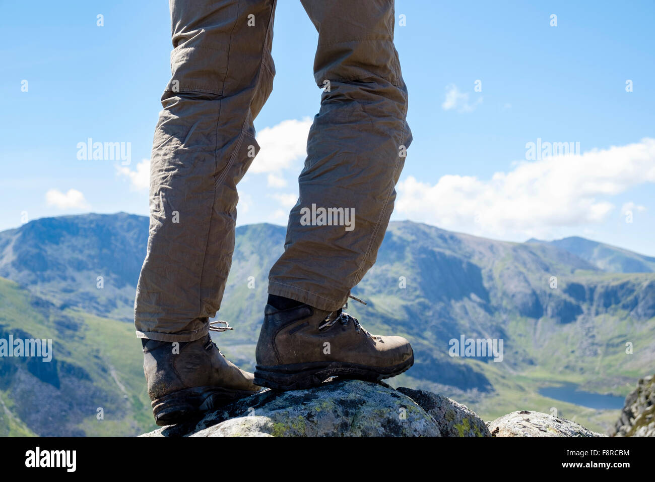 Hiker's legs wearing walking boots hiking on Carnedd Pen yr Ole Wen with view to Glyders and Snowdon in distance. Snowdonia National Park Wales UK Stock Photo