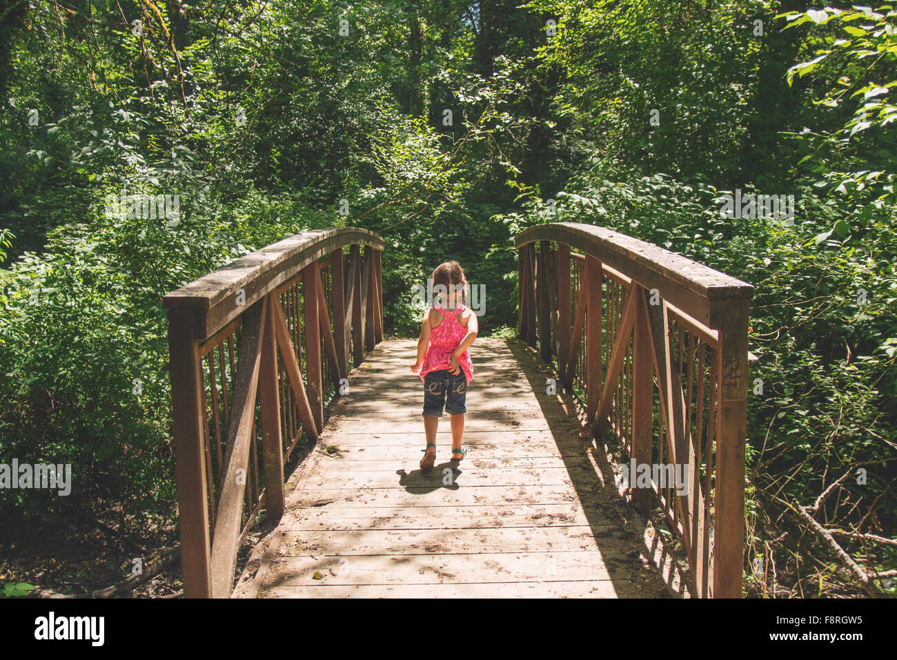 Young girl walking across bridge in woods Stock Photo