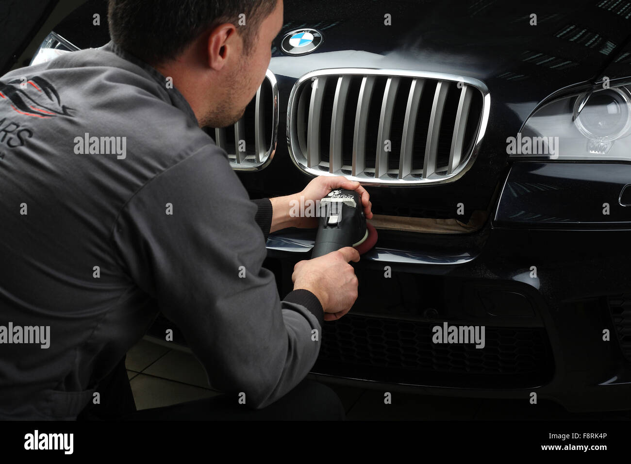 Illustrative editorial. The worker polishes a bumper car cowl with the
