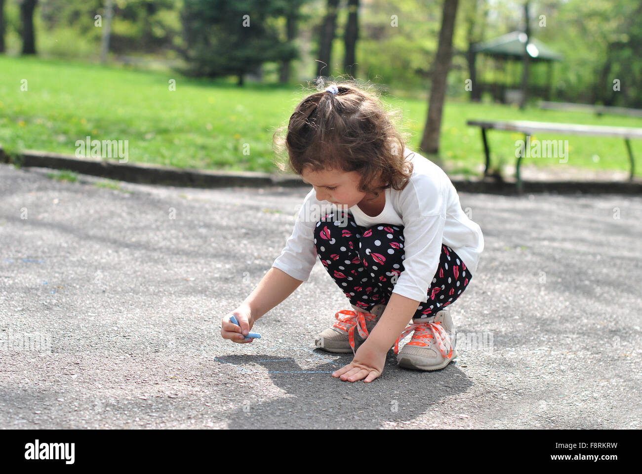 Girl drawing hopscotch on road with chalk Stock Photo