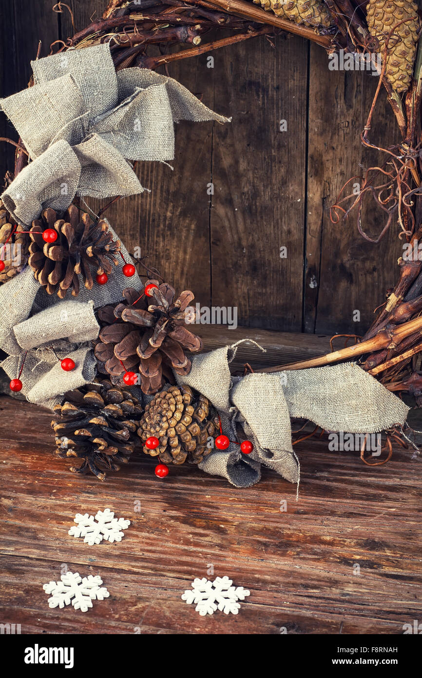 Woven from twigs and decorated with pine cones Christmas wreath on wooden background. Stock Photo