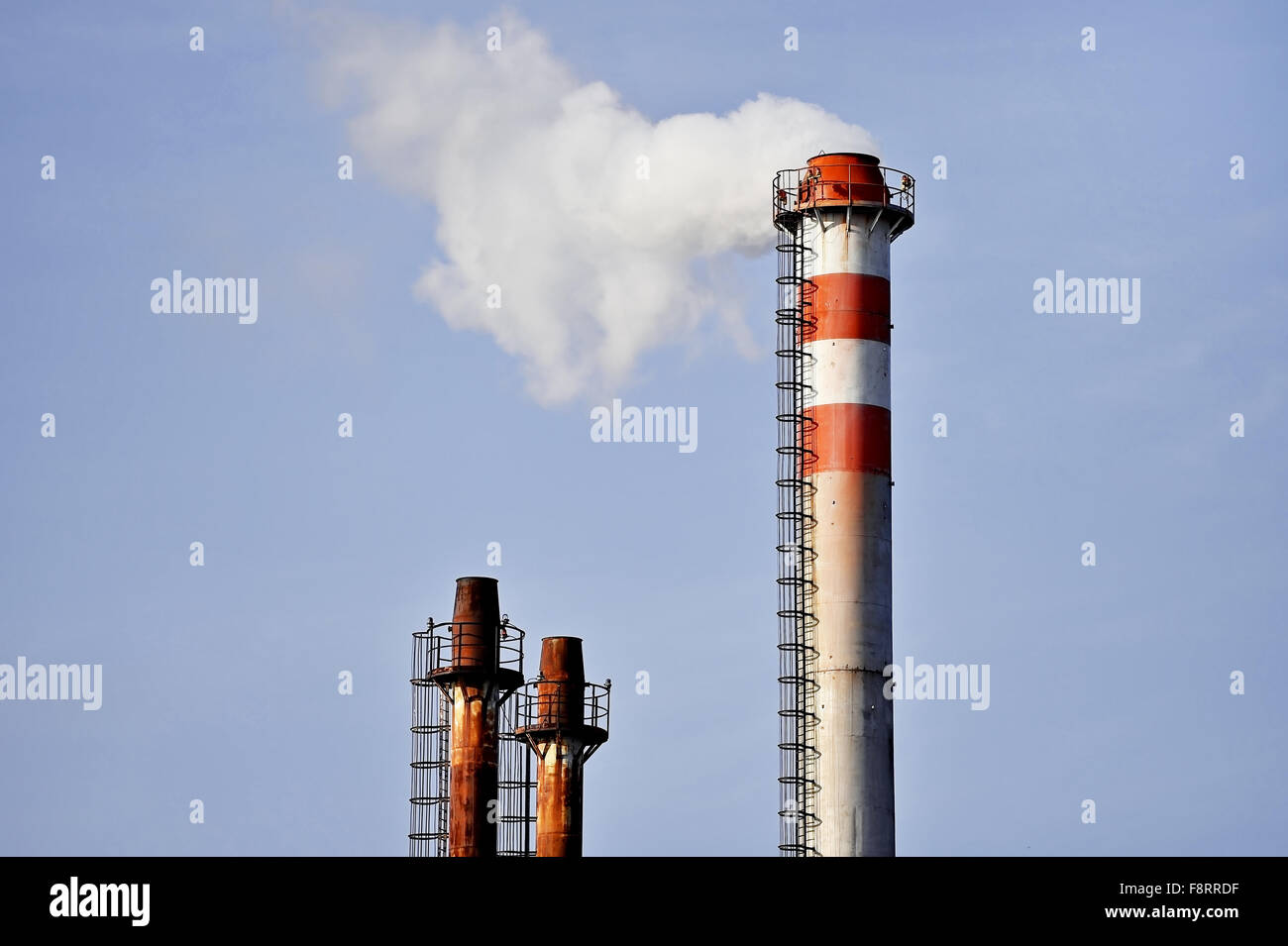 Smoke and steam coming out from an industrial petrochemical plant chimney with a blue sky on the background Stock Photo