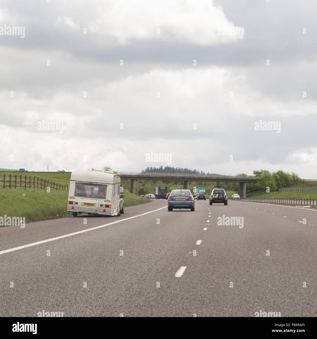 damaged caravan with buckled collapsed wheel pulled up on the hard shoulder of the motorway in Scotland, UK Stock Photo