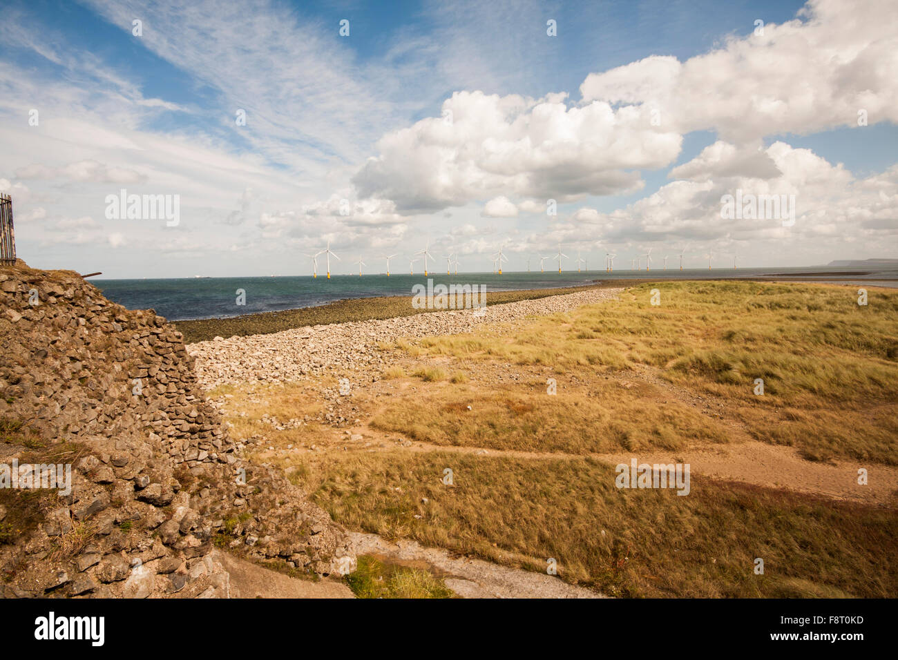A view of the wind turbines off the east coast at Redcar showing rocky shoreline and blue cloudy skies Stock Photo