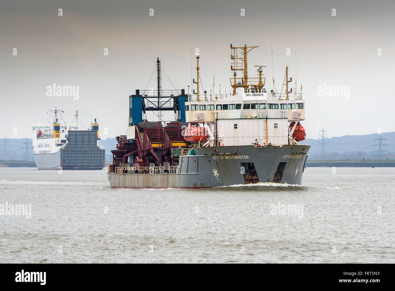 The dredger City of Westminster passes an outward bound Cobelfret Ferry as she steams upriver on the River Thames. Stock Photo