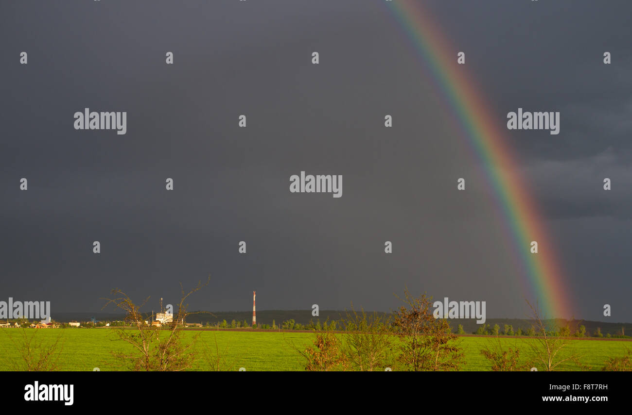 The dramatic rainbow against the dark clouds and the unusual color of the sun Stock Photo