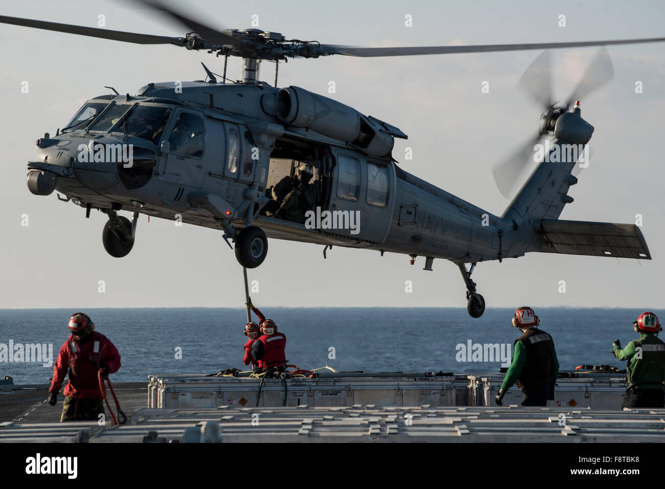 Sailors connect a cargo pendant to an MH-60S Seahawk, Sikorsky SH-60/MH-60 Seahawk, from the “Island Knights” of Helicopter Sea Combat Squadron (HSC) 25 on the flight deck of the U.S. Navy's only forward-deployed aircraft carrier USS Ronald Reagan. Stock Photo