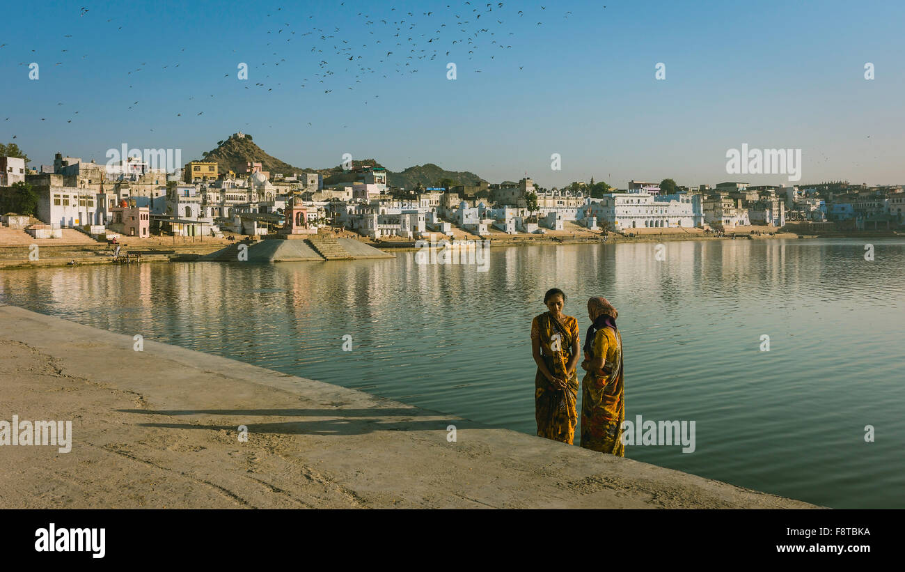 Hindu pilgrims arrive for a bath in the holy lake at dawn with houses and hills as backdrop. Stock Photo
