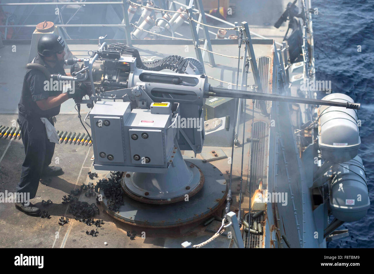 Gunner's Mate 1st Class fires an Mk-38 25mm chain gun during a live-fire exercise aboard the guided-missile destroyer USS Farragut (DDG 99). Stock Photo