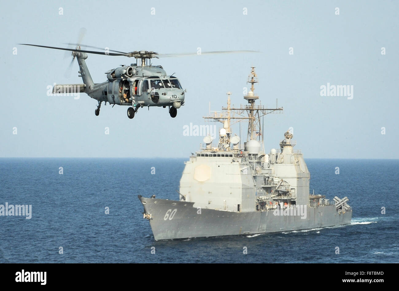 HH-60H Sea Hawk helicopter assigned to the Sea Knights of Helicopter Sea Combat Squadron (HSC) 22 passes the guided-missile cruiser USS Normandy Stock Photo