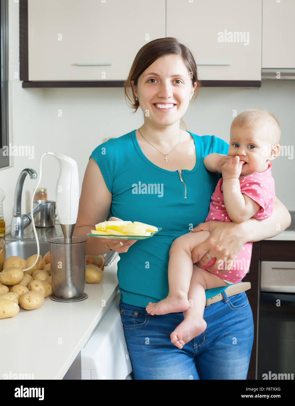 Young woman and baby girl cooking mashed potatoes with blender in kitchen Stock Photo