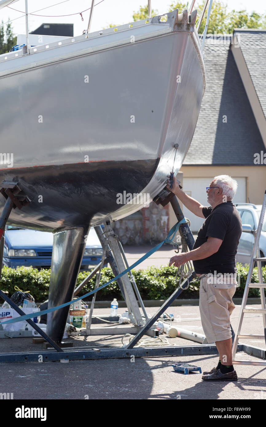 A man is painting the underside hull of a boat in a dock yard in