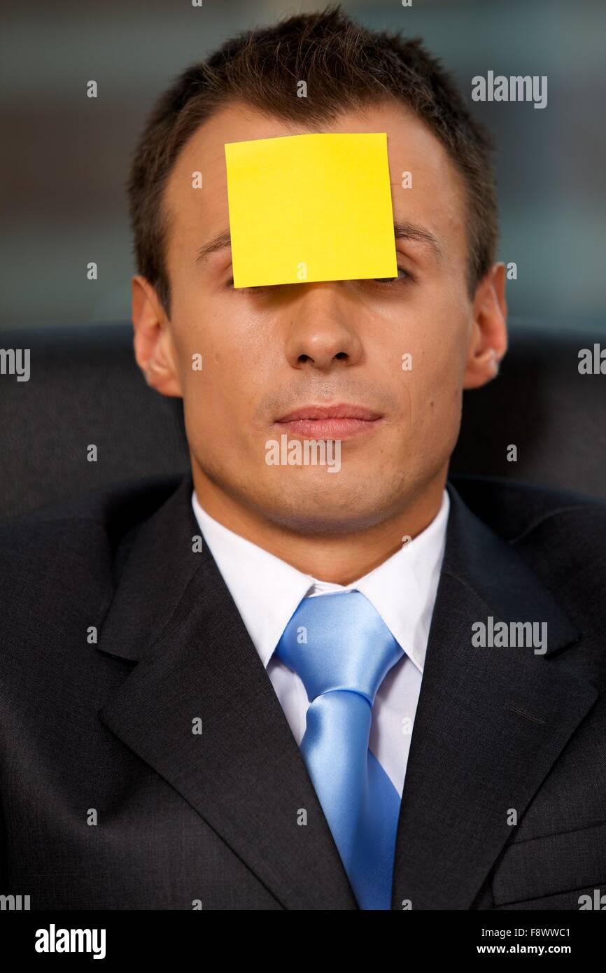 Businessman in office with blank adhesive note stuck to forehead Stock Photo