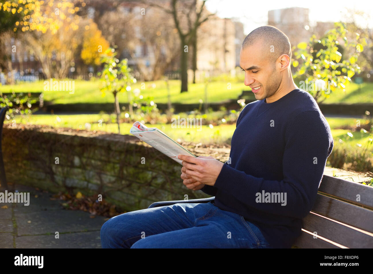 Young man sitting on a park bench reading a magazine Stock Photo - Alamy
