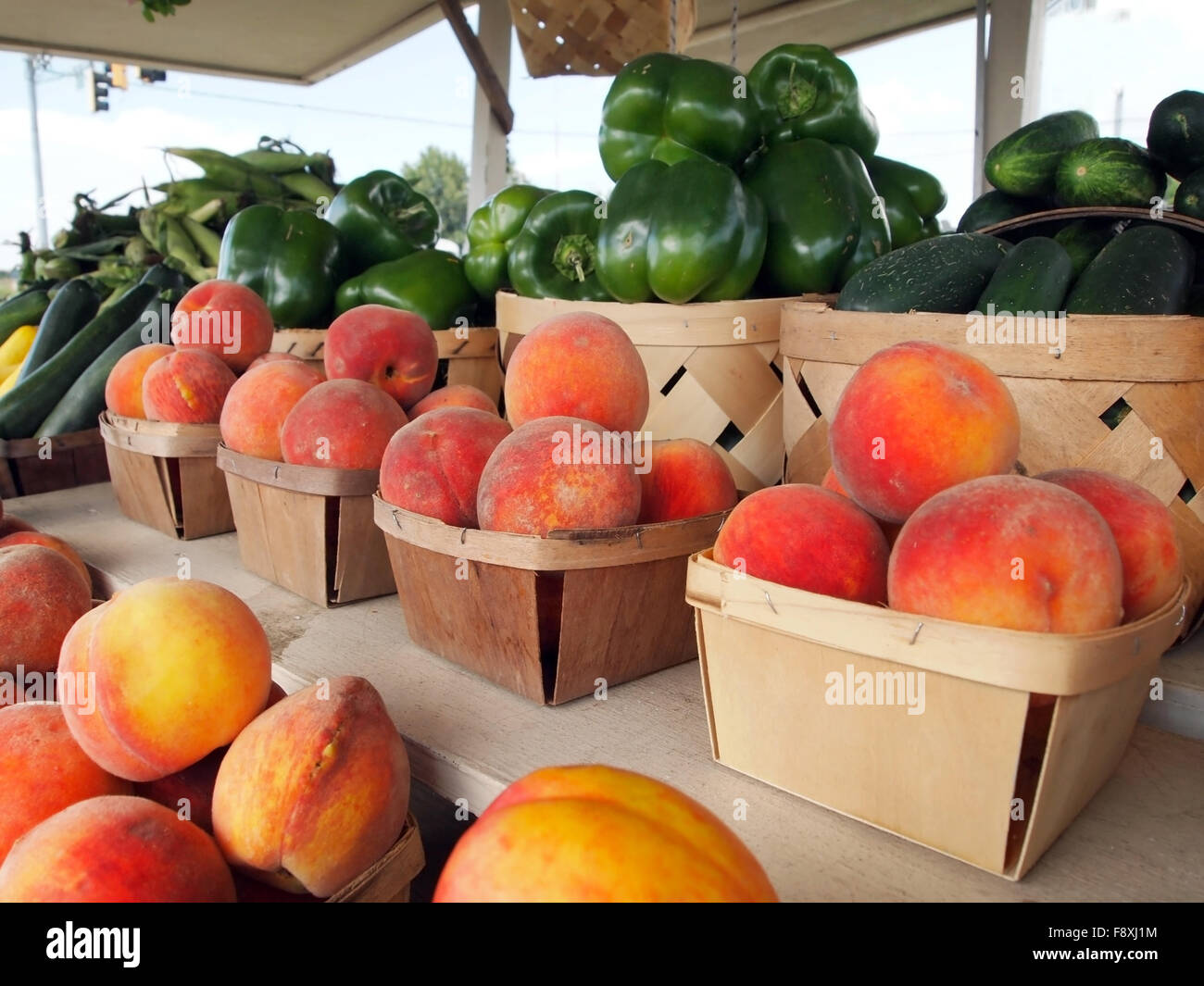 Baskets of peaches in rows at a roadside produce stand wtih bell peppers, corn and squash in the background. Stock Photo