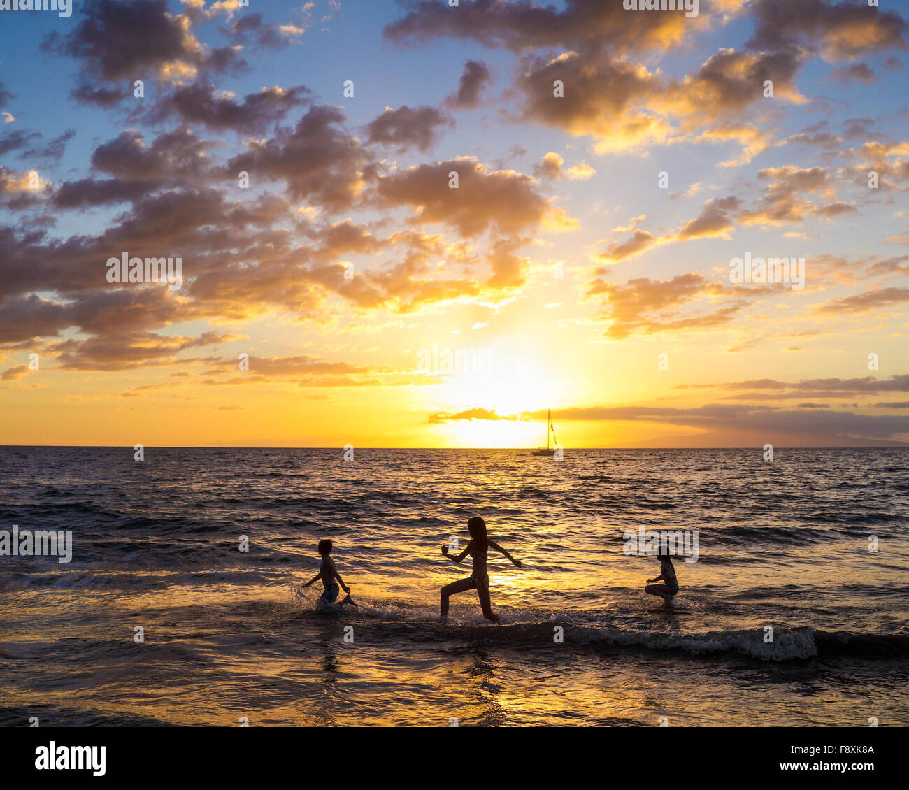 Kids in Kihei, Maui, run in the surf at sunset Stock Photo