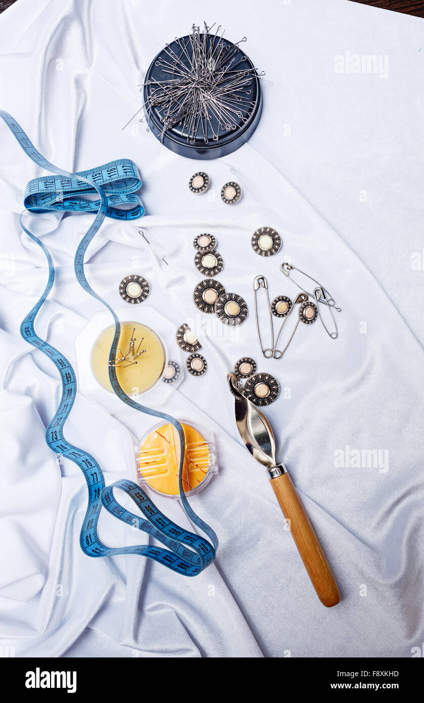 Buttons, pins, measuring tape and needles lying on the silk. The