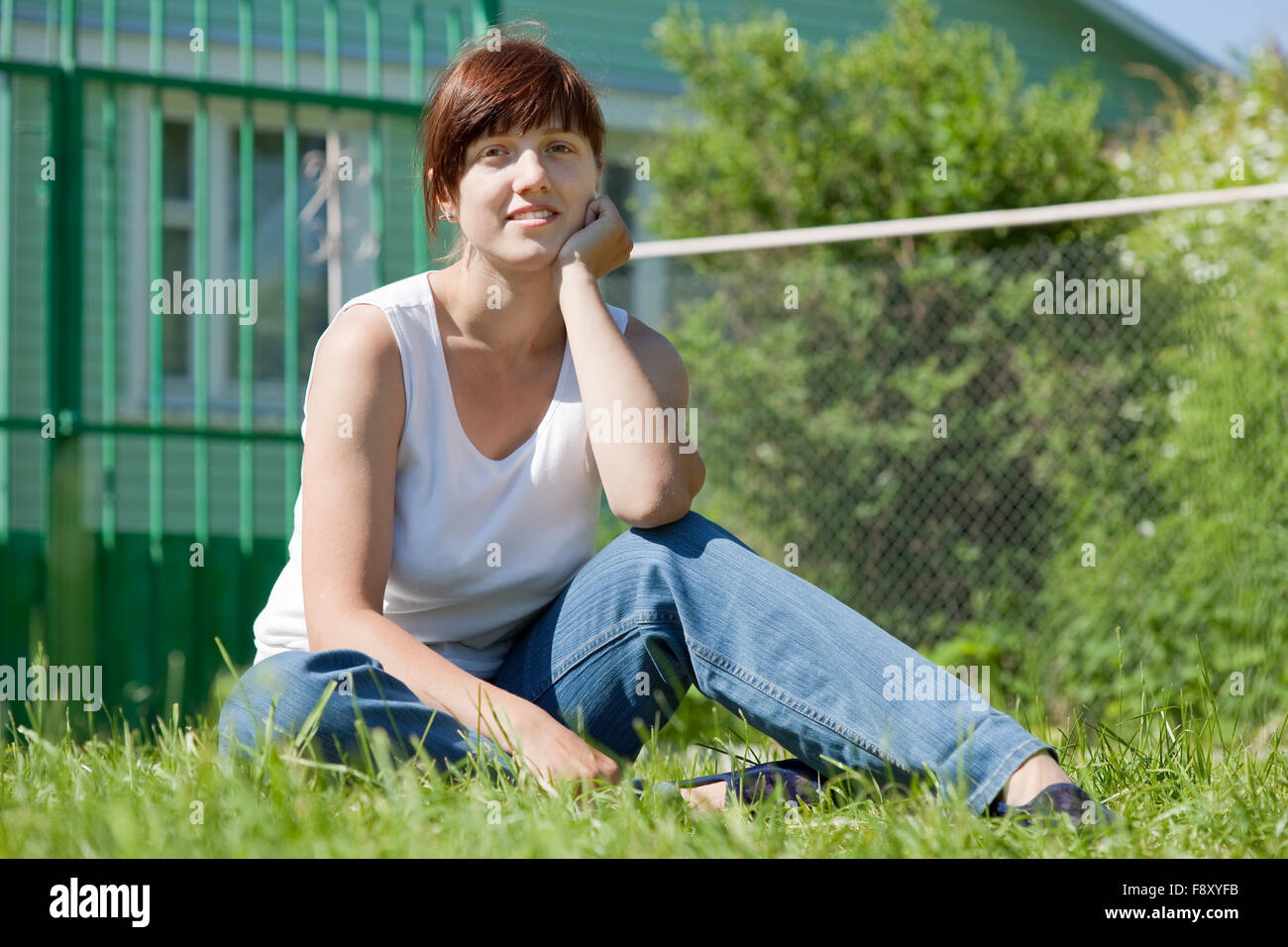 Happy young woman sitting on lawn in front of new home Stock Photo - Alamy