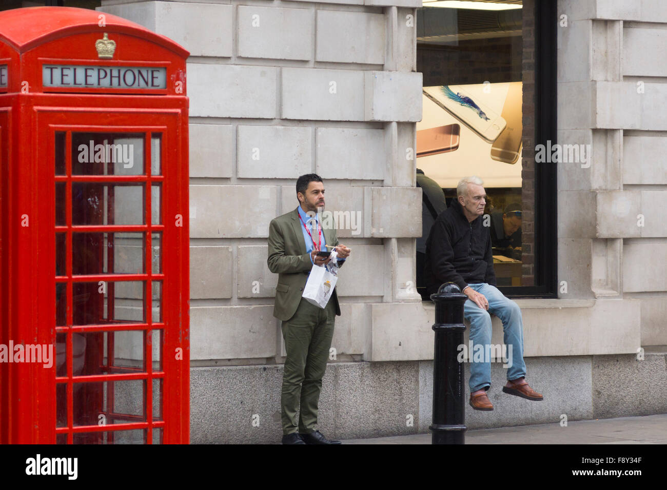 A man eating lunch standing up and a man sitting down smoking in London Stock Photo