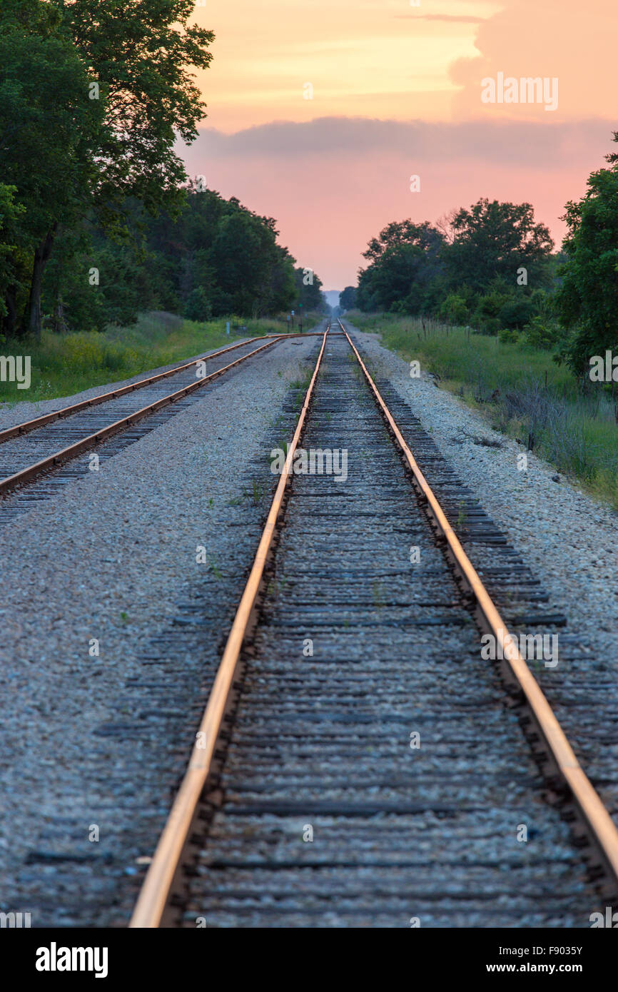 Long straight railroad tracks running into the distance at sunset with warm colors in sky and reflecting on tracks Stock Photo
