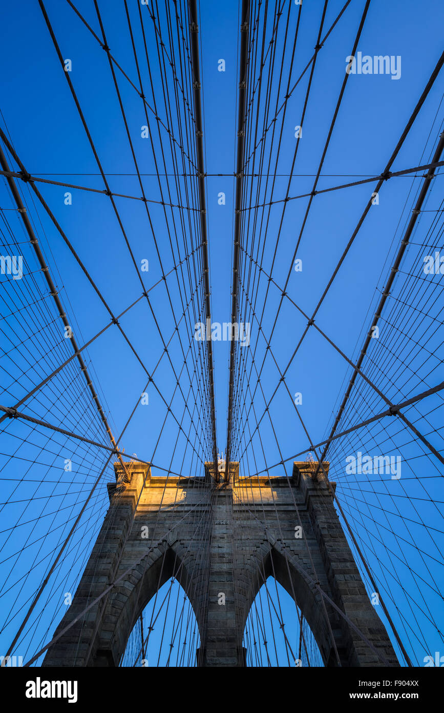 Brooklyn Bridge tower with double gothic arches and symmetrical suspension cables at sunset with clear blue sky, New York City Stock Photo