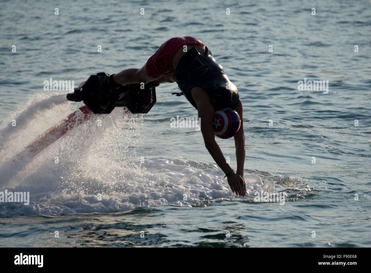 Flyboarder in silhouette diving into calm sea Stock Photo