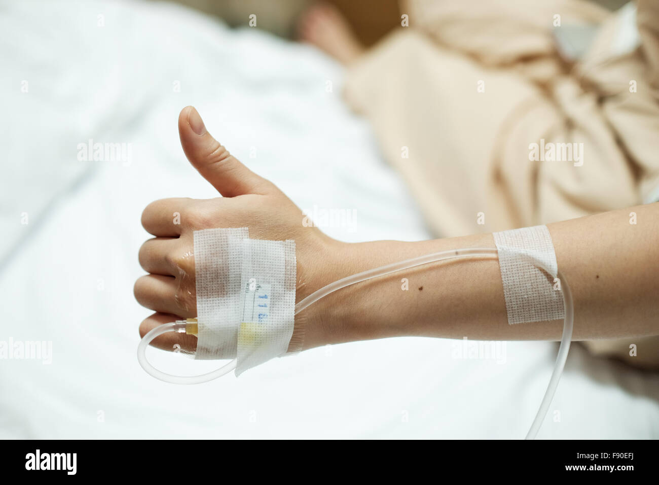 Patient hand thumbs up while given saline IV drip injection on hospital bed, medical or health concept Stock Photo