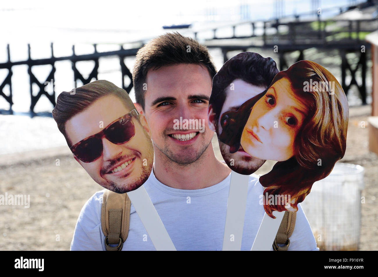 Young man holding fun face masks on beach, Southend-On-Sea, Essex, England, United Kingdom Stock Photo