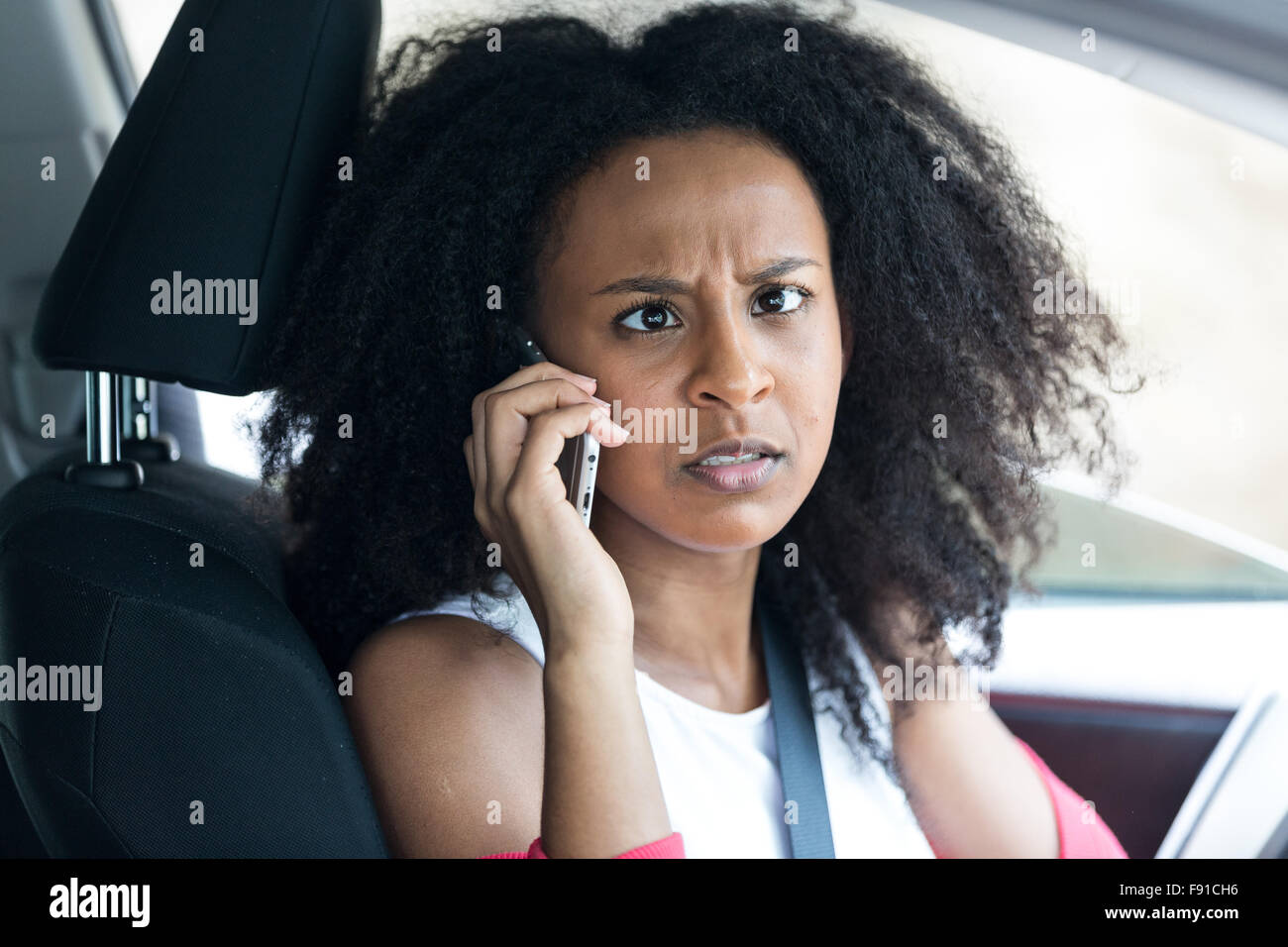 An attractive mixed race young woman in a car chatting on her mobile phone looking cross eyes and crazy Stock Photo