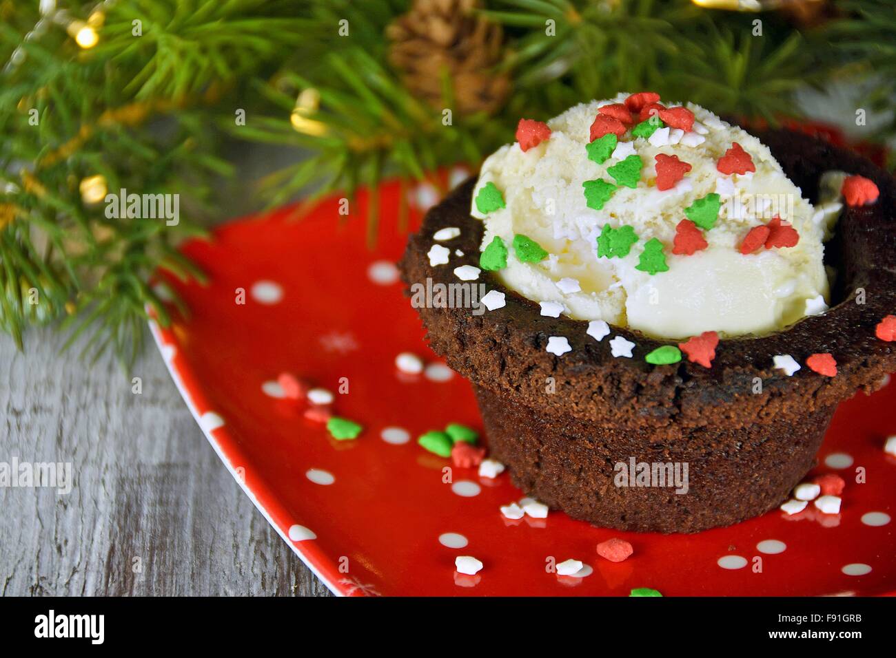 Christmas candy sprinkles on vanilla ice cream in brownie cup on red plate with holiday decorations. Stock Photo