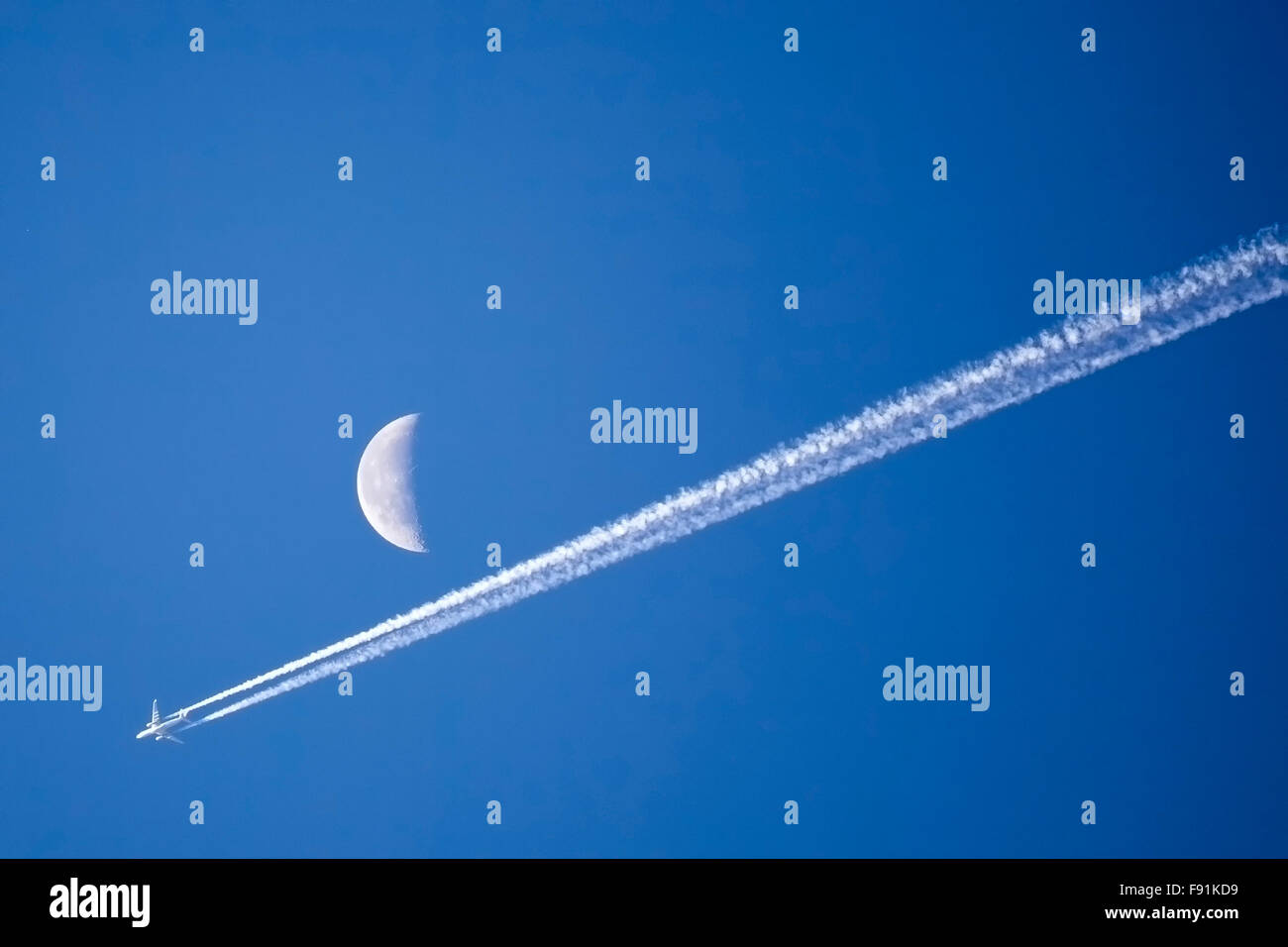 Airplane Flying Past The Moon Against Bright Blue Sky Stock Photo