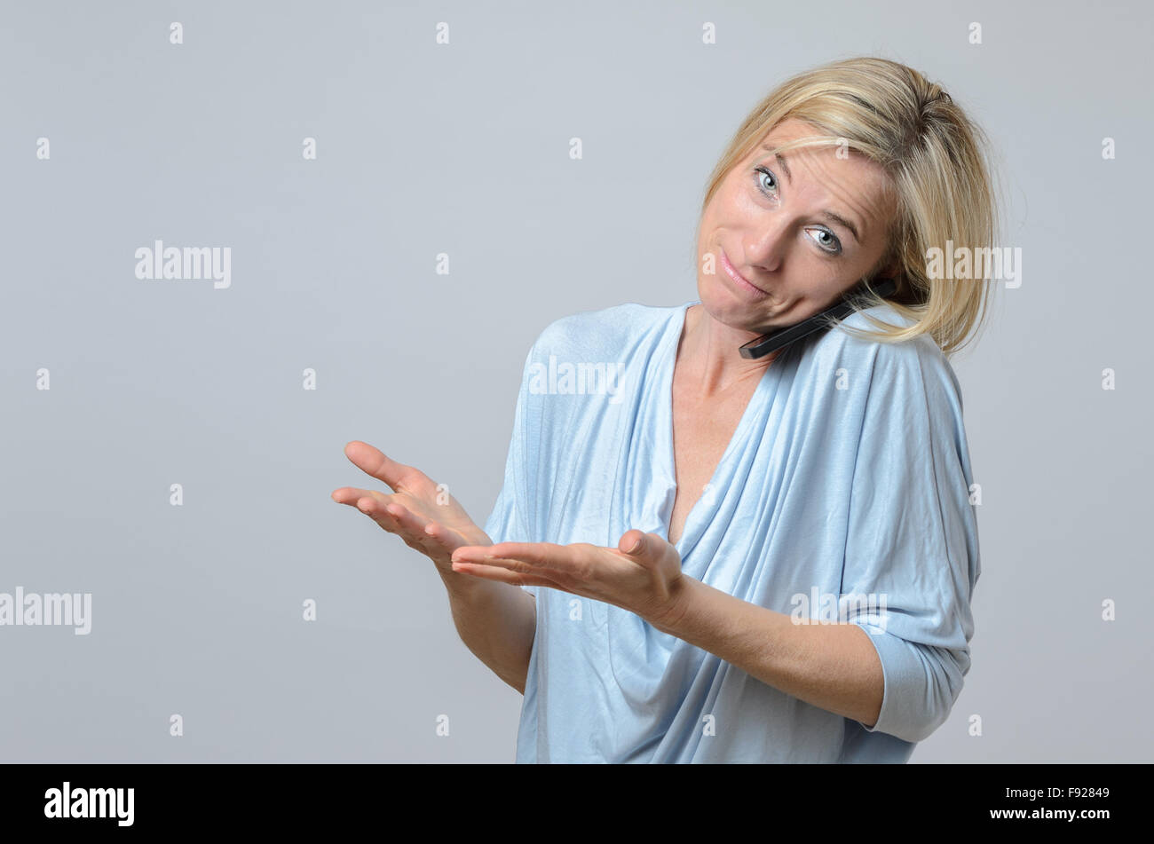 Attractive blond woman standing shrugging her shoulders in ignorance, indifference or confusion with a wry smile Stock Photo