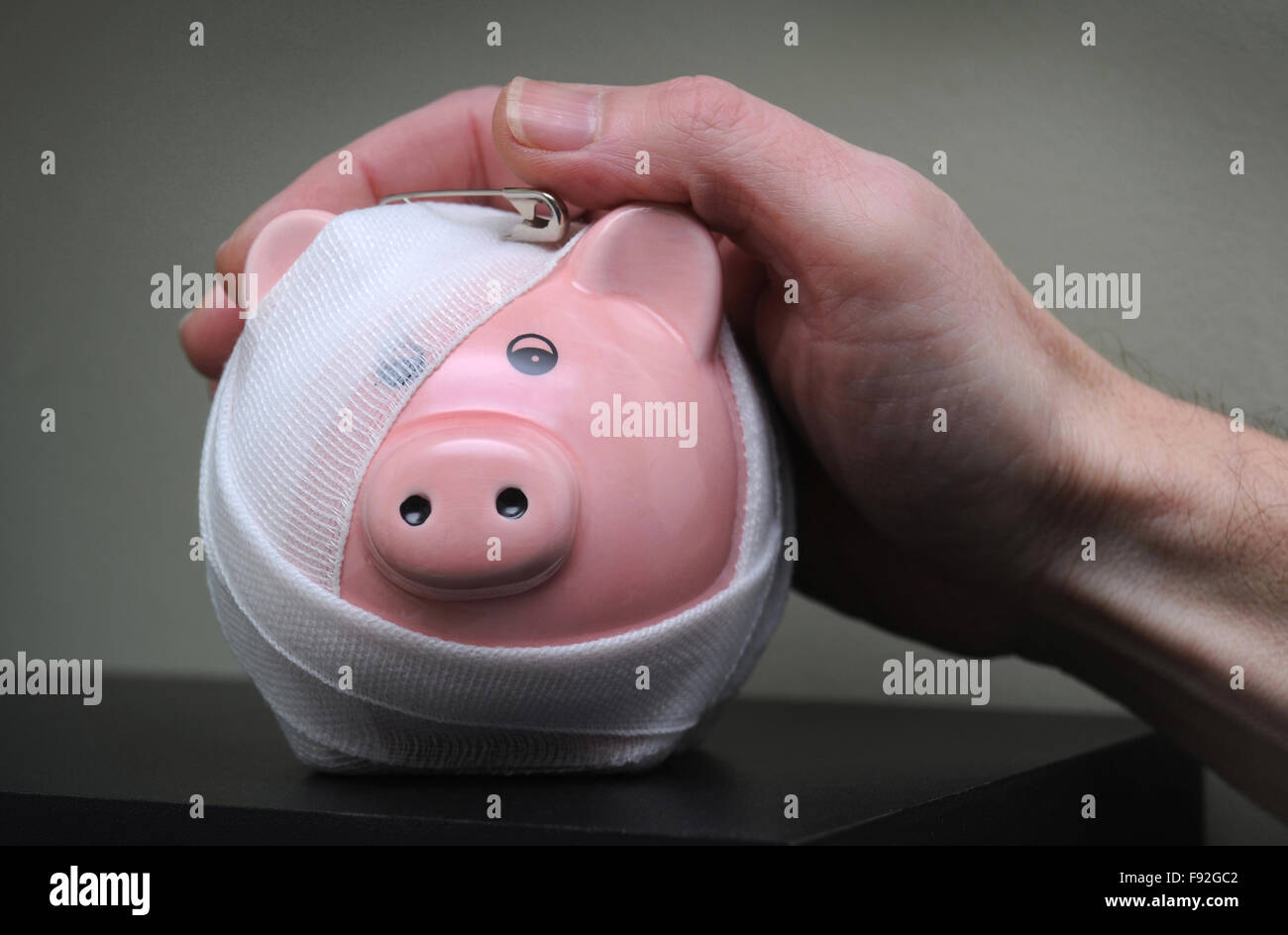 BANDAGED PIGGYBANK WITH MANS HAND RE INVESTMENTS PIGGY BANK PRIVATE PENSION COMPANY STATE PENSIONERS MORTGAGES SAVINGS MONEY UK Stock Photo