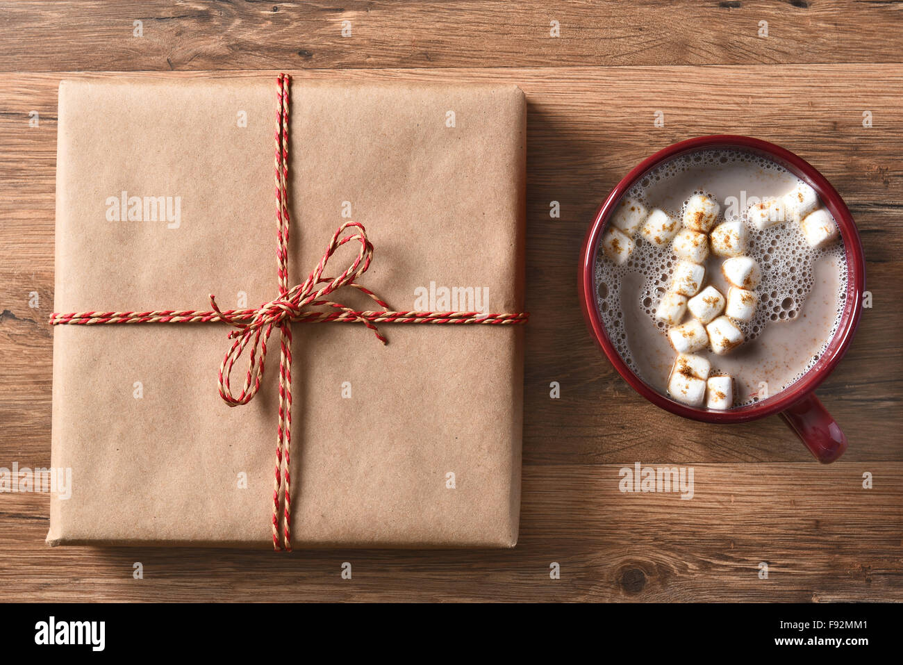 High angle view of a plain brown paper wrapped Christmas Present next to a large mug of hot cocoa with marshmallows. Stock Photo