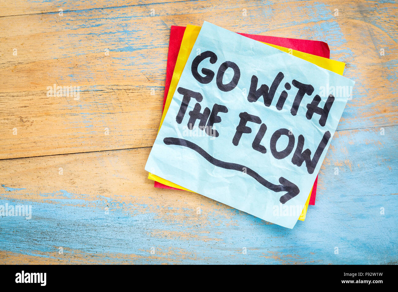 Go with the flow advice or reminder on a sticky note against grunge painted wood Stock Photo