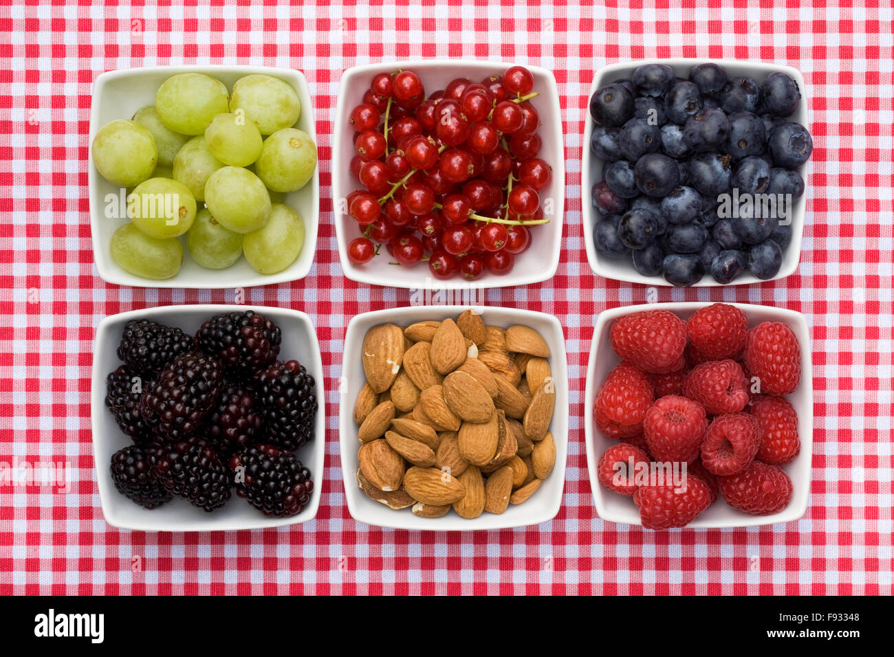 Redcurrants, Grapes, Blackberries, Almonds, Raspberries and Blueberries in white bowls on a checked background. Stock Photo