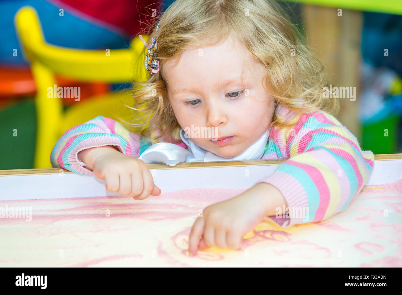 Cute child girl drawing draws developing sand in preschool at table in