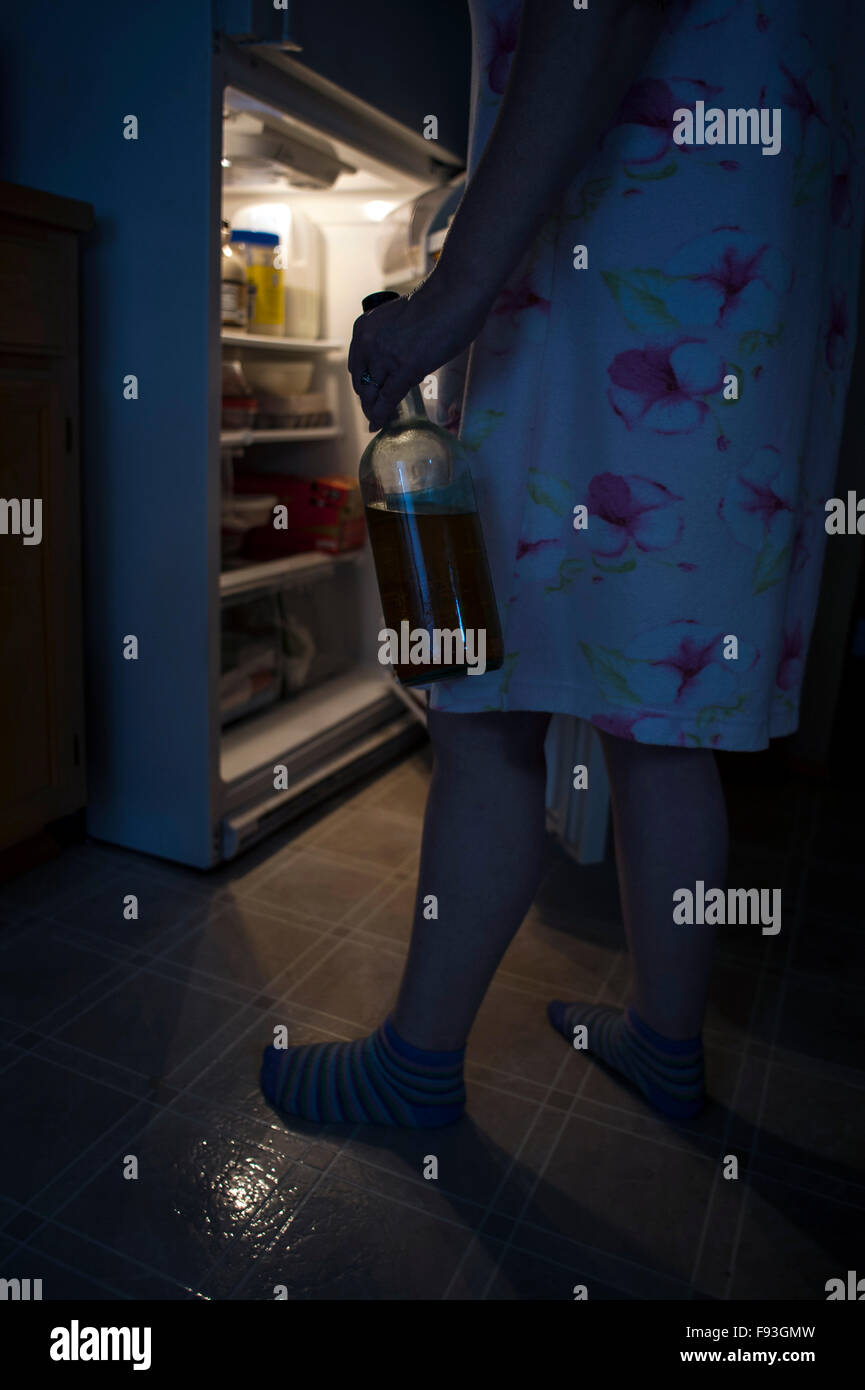 Woman opening refrigerator door at night to get a snack holding a bottle Stock Photo
