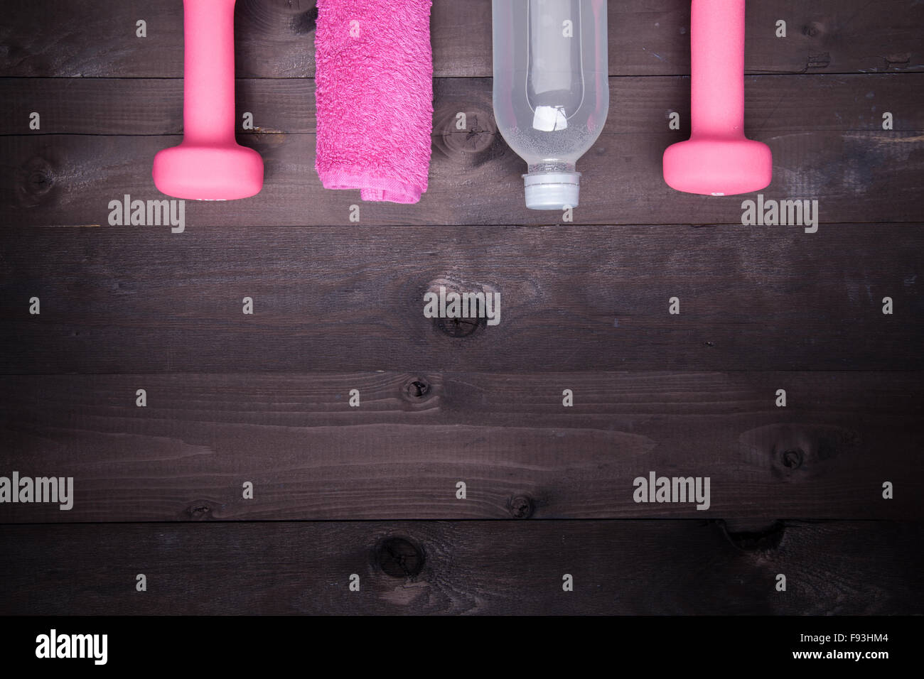 Sport equipment. Water bottle, pink towel and a  pink dumbbell on a black wooden background Stock Photo